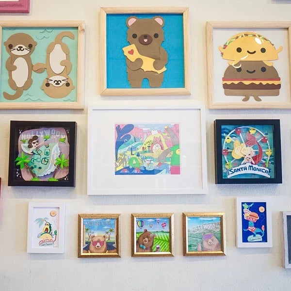 Close-up photo of gallery wall from the "California Love" art show. Art features things such as bears, otters, tacos, and the hollywood sign. 