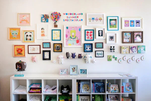 Photo of the gallery wall for the "Wonderland Summer Spectacular" art show featuring over thirty art pieces. All art is cute and bright featuring animals, balloons, and more.