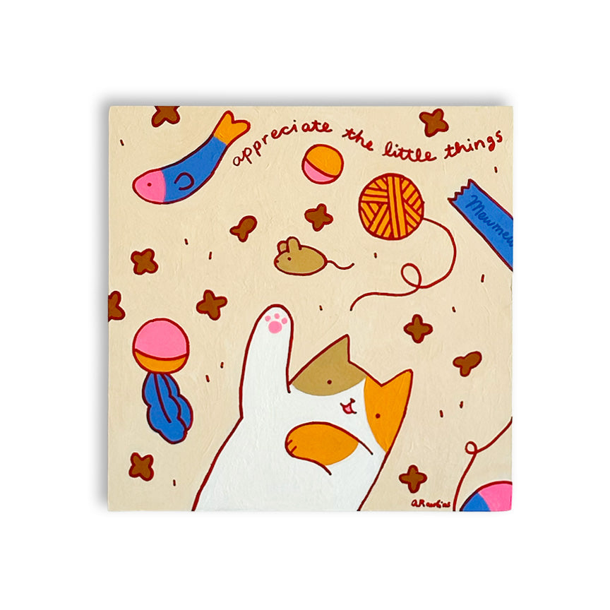 A square canvas featuring a whimsical cat and toy illustration on a light beige background. The illustration includes a white cat with orange and brown patches, a blue fish, a yellow ball, a blue toy, and the text "appreciate the little things."
