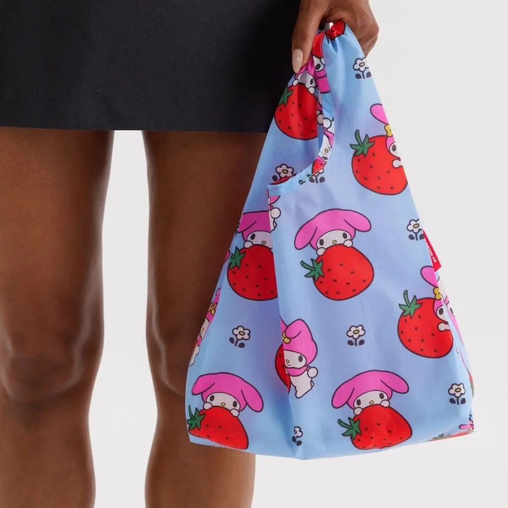 Light blue reusable bag with cartoon character and strawberry pattern held by a person.
