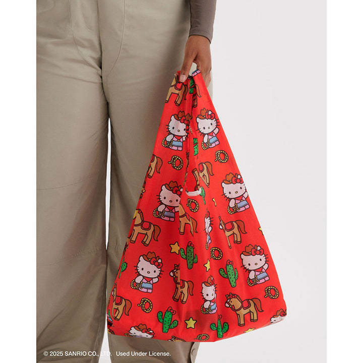 Red bag with Hello Kitty and horse pattern held by a person wearing beige pants.