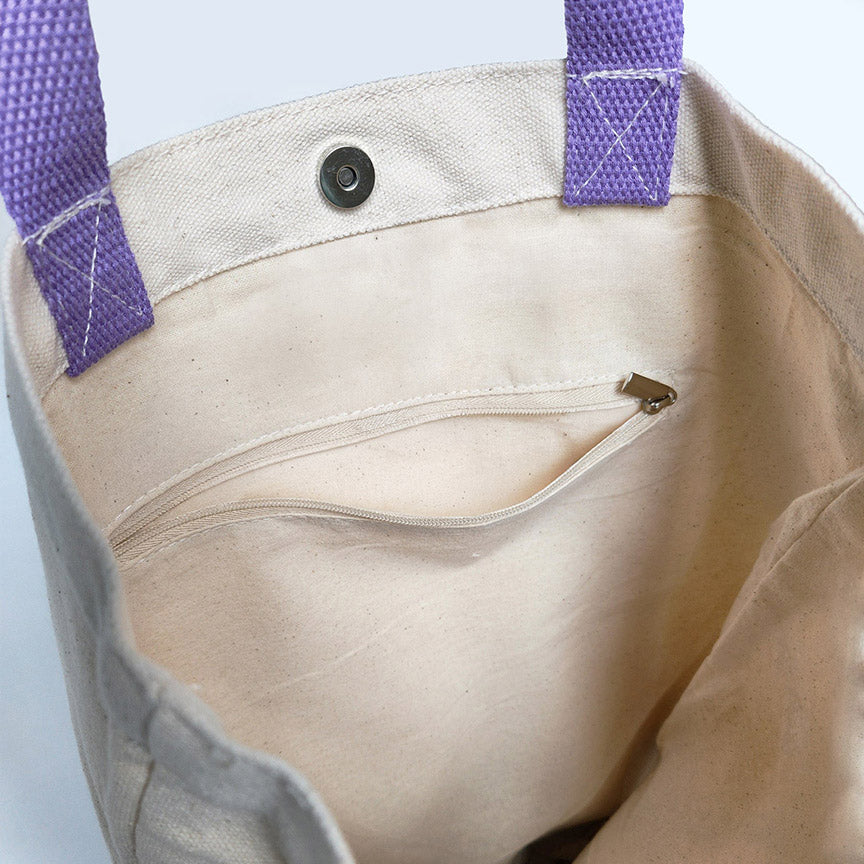 Close-up of a beige tote bag with purple straps on a light gray background.