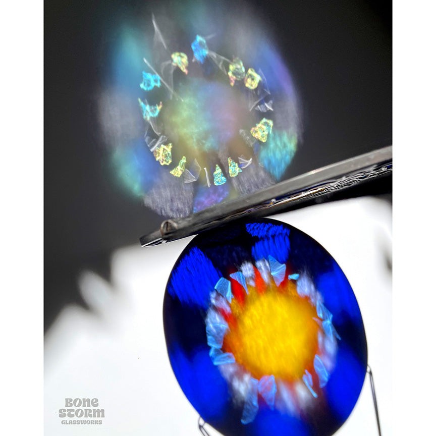 Colorful reflection on wall of a bright circular stained glass suncatcher featuring a deep blue glass and yellow and orange sun design.