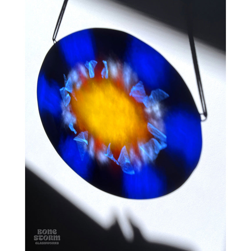 Colorful reflection on wall of a bright circular stained glass suncatcher featuring a deep blue glass and yellow and orange sun design.