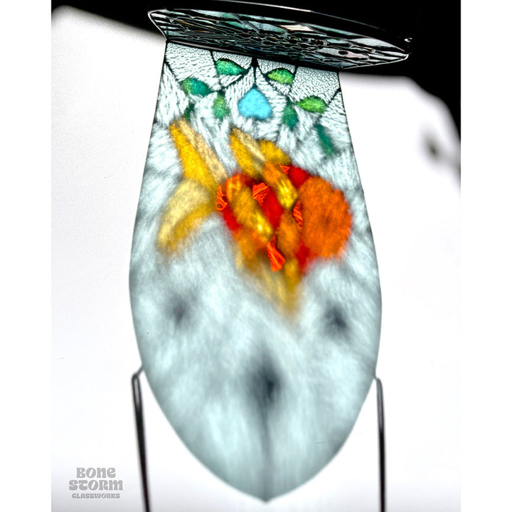 Reflection on the wall of a bright stained glass suncatcher featuring an orange goldfish design, hanging by a black cloth string near a window with bright sunlight and shadows. 