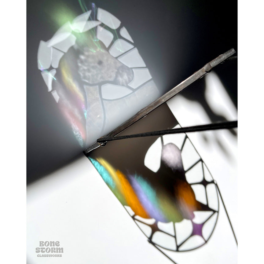 Colorful double reflection on floor of a stained glass suncatcher with a white and pastel rainbow unicorn design. Design is such that the shadow on the ground looks like that of a unicorn in profile. 