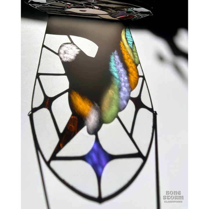 Colorful reflection on a wall of a stained glass suncatcher with a white and pastel rainbow unicorn design. Design is such that the shadow on the wall looks like that of a unicorn in profile. 