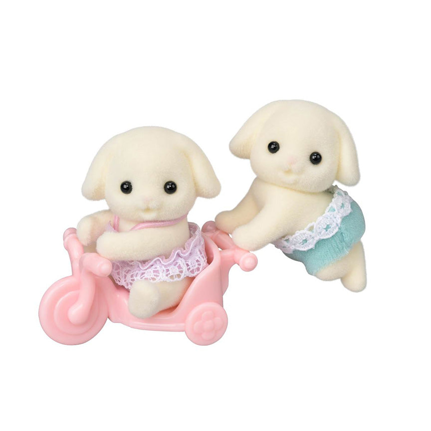 Two felted bunny rabbit toys with floppy ears. One is crawling wearing blue shorts while the other is in a pink plastic tricycle wearing a pink dress. 