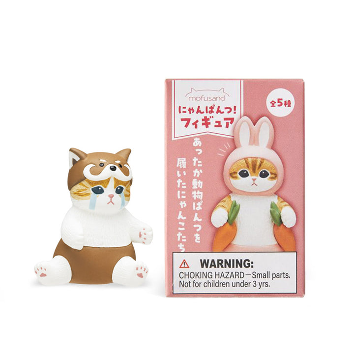 A blind box package featuring a cute cat in various outfits with pastel colors. A crying cat figurine in pants and hat with a face on it is displayed beside the package.