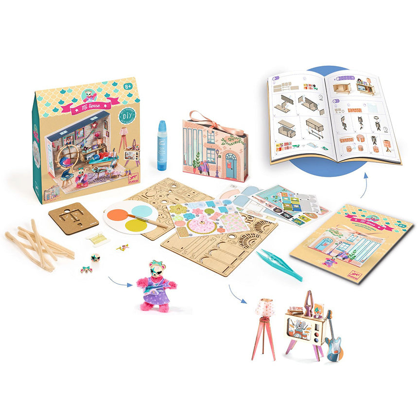 Djeco DIY craft kit displayed on a white background, showing the colorful retail box, a small storage box, an open instruction booklet, a paint palette, wooden sticks, small accessories, and assembled toy scenes including a doll, a small house, and an easel.