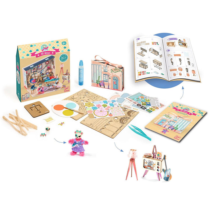 Djeco DIY craft kit displayed on a white background, showing the colorful retail box, a small storage box, an open instruction booklet, a paint palette, wooden sticks, small accessories, and assembled toy scenes including a doll, a small house, and an easel.