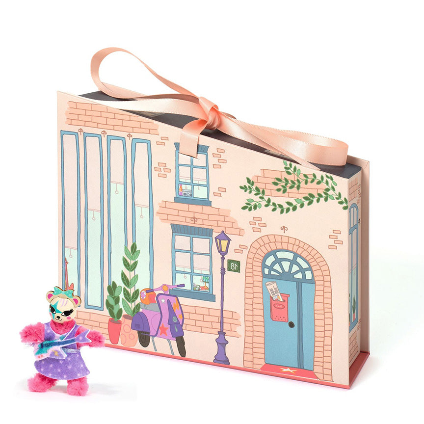Dejco toy bear figure in front of a decorative box with a street scene that looks like the outside of a house. 