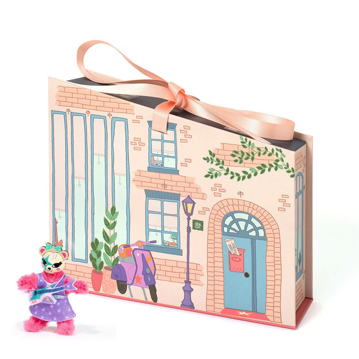 Dejco toy bear figure in front of a decorative box with a street scene that looks like the outside of a house. 