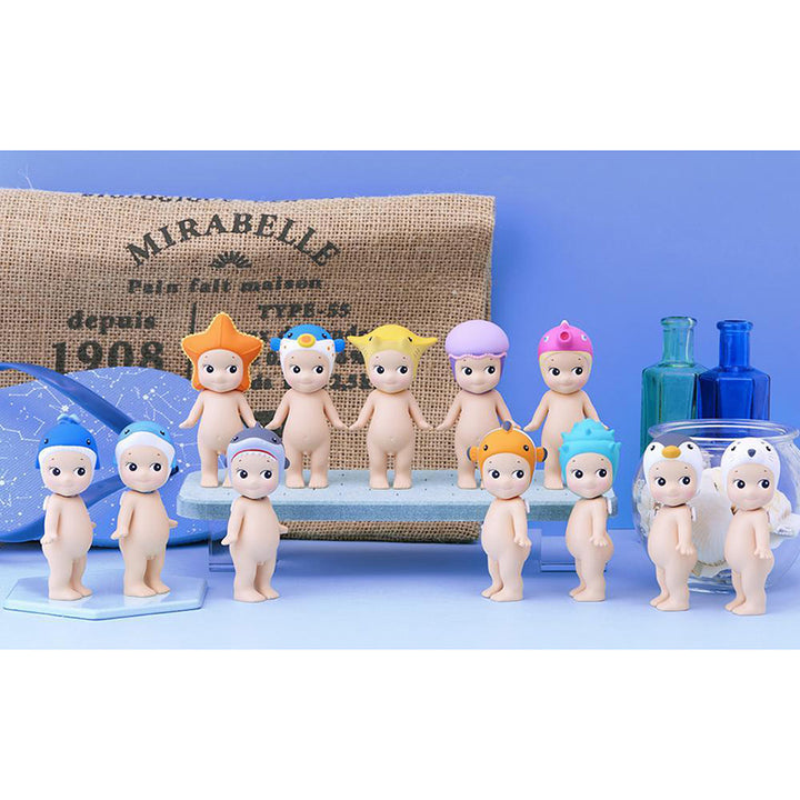 Set of small figurines with colorful marine animal hats on a blue surface with a burlap bag in the background.