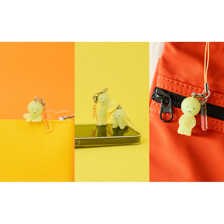 Set of three photos with examples of Smiski keychain uses; Attached to the zipper of a pencil case, on the bottom of a phone case, and dangling from a backpack strap.