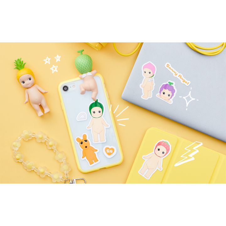 A flat-lay product photo of a light blue phone case decorated with cute cartoon stickers and 3D character figures, shown alongside matching yellow accessories on a pastel yellow background.