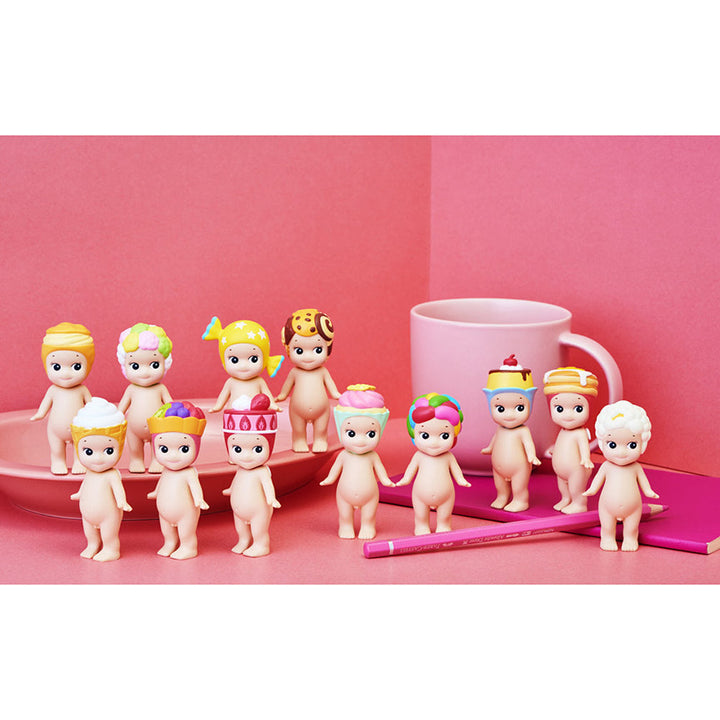 A collection of sweets-themed figurines on a pink background with a pink plate, notebook, and mug.