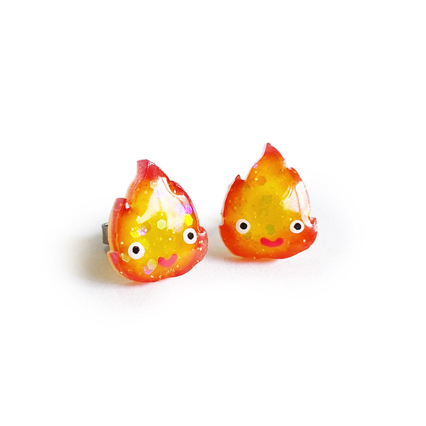 A pair of sparkly fire-shaped stud earrings with cute faces, in the style of the character Calcifer from the movie "Howl's Moving Castle."