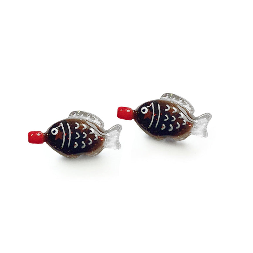 A pair of fish-shaped soy sauce packet stud earrings featuring a glossy dark brown body with red star glitter inside, white scale details, and a small red mouth or &