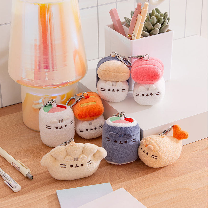 Set of Pusheen plush keychains on a desk with stationery items.