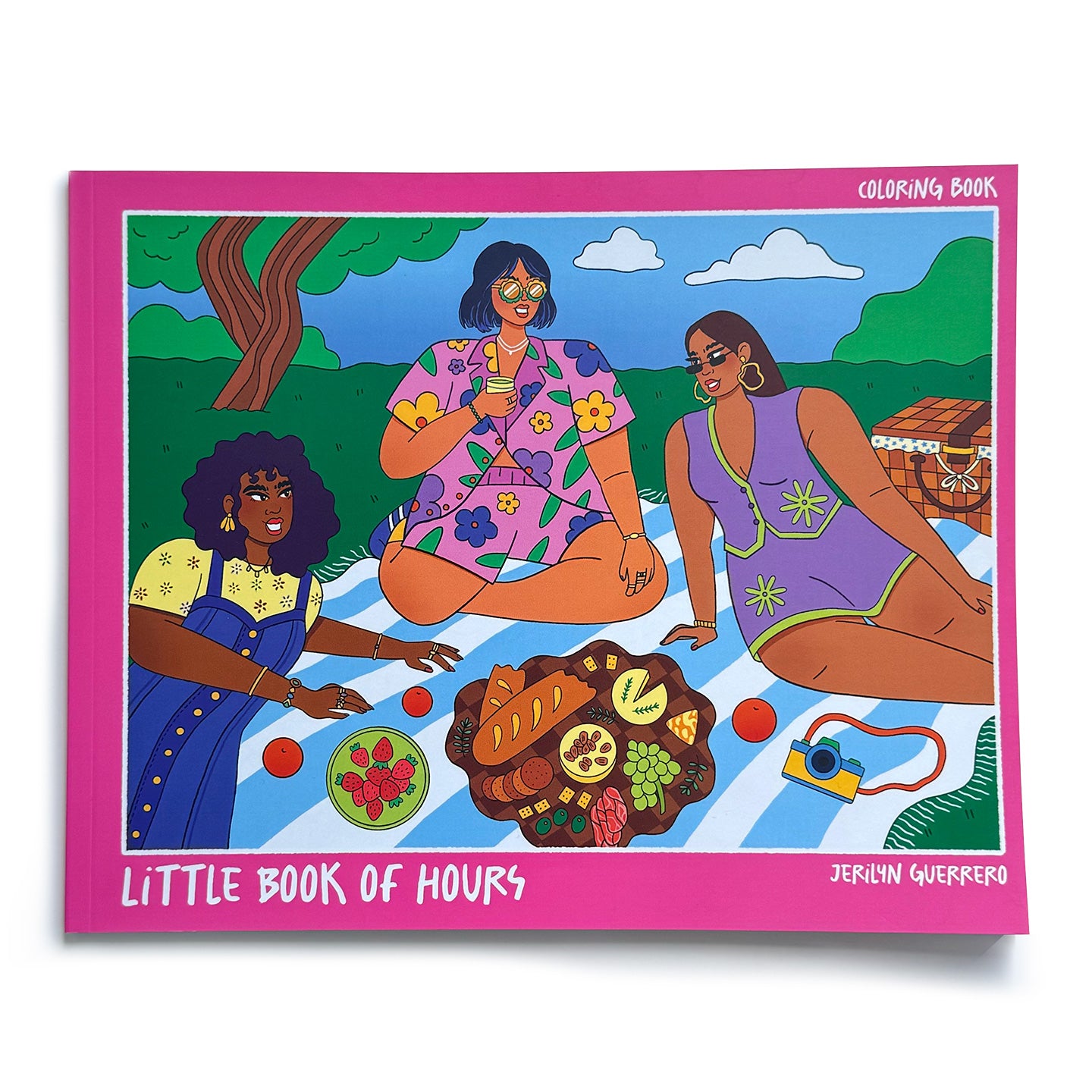 Coloring book with a hot pink border featuring a colored-in image of three girls of different skin tones (shades of black and brown) sitting at a picnic in the park. Book is titled "Little Book of Hours". 
