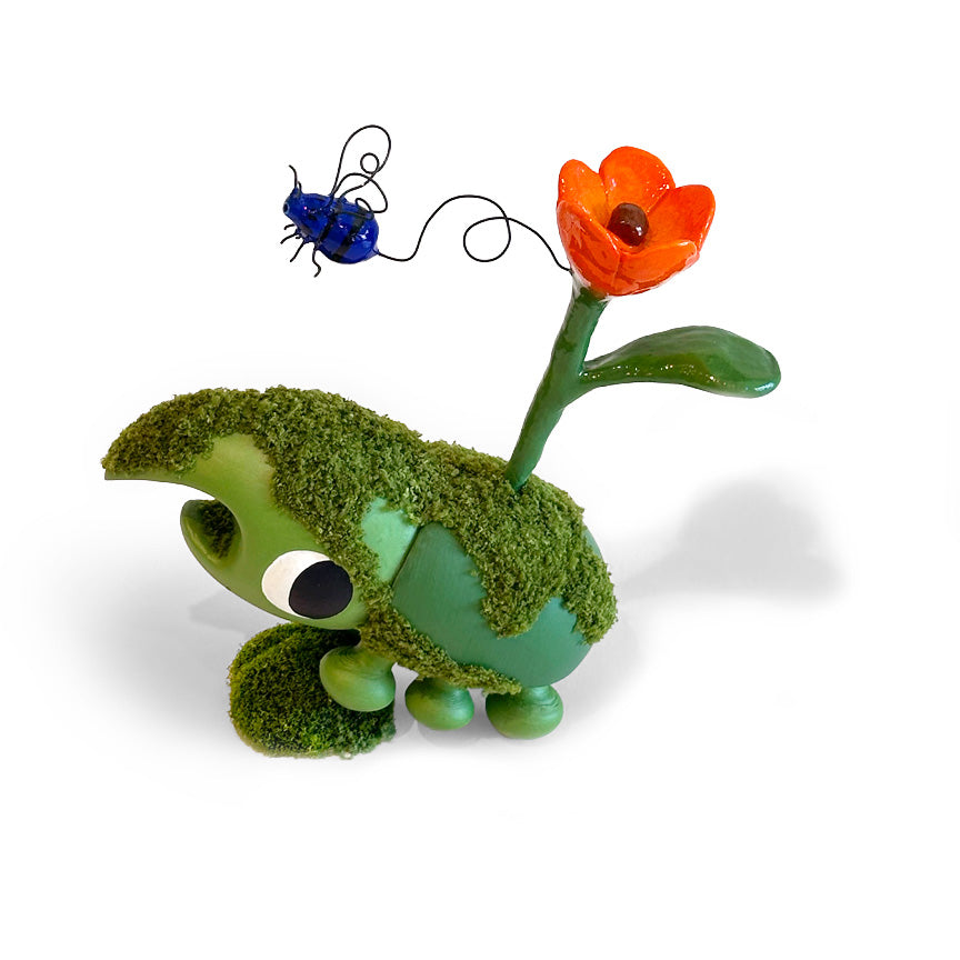 A whimsical green bug sculpture covered in faux moss, with a bright orange flower on a stem and a small blue wire beetle above it, photographed on a clean white background.