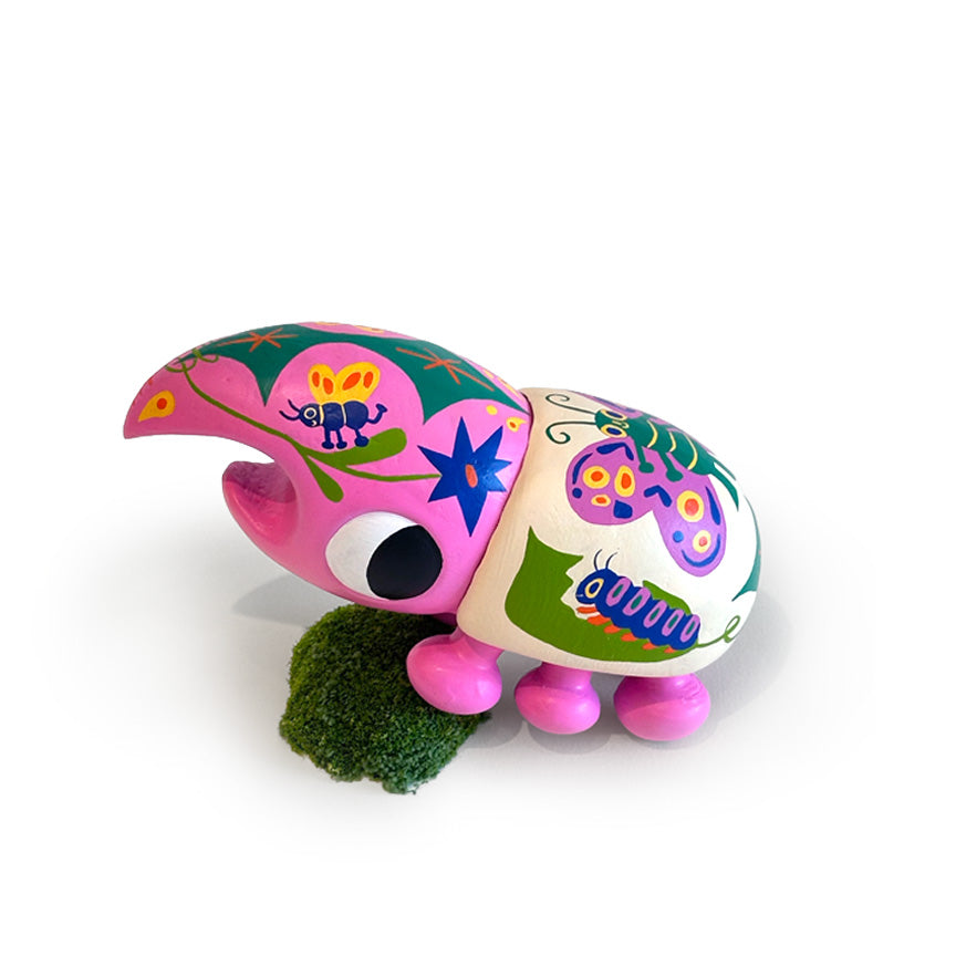 A colorful beetle sculpture with hand-painted floral and insect motifs in pink, green, purple, blue, yellow, and white, standing on a small green mossy base against a plain white background.