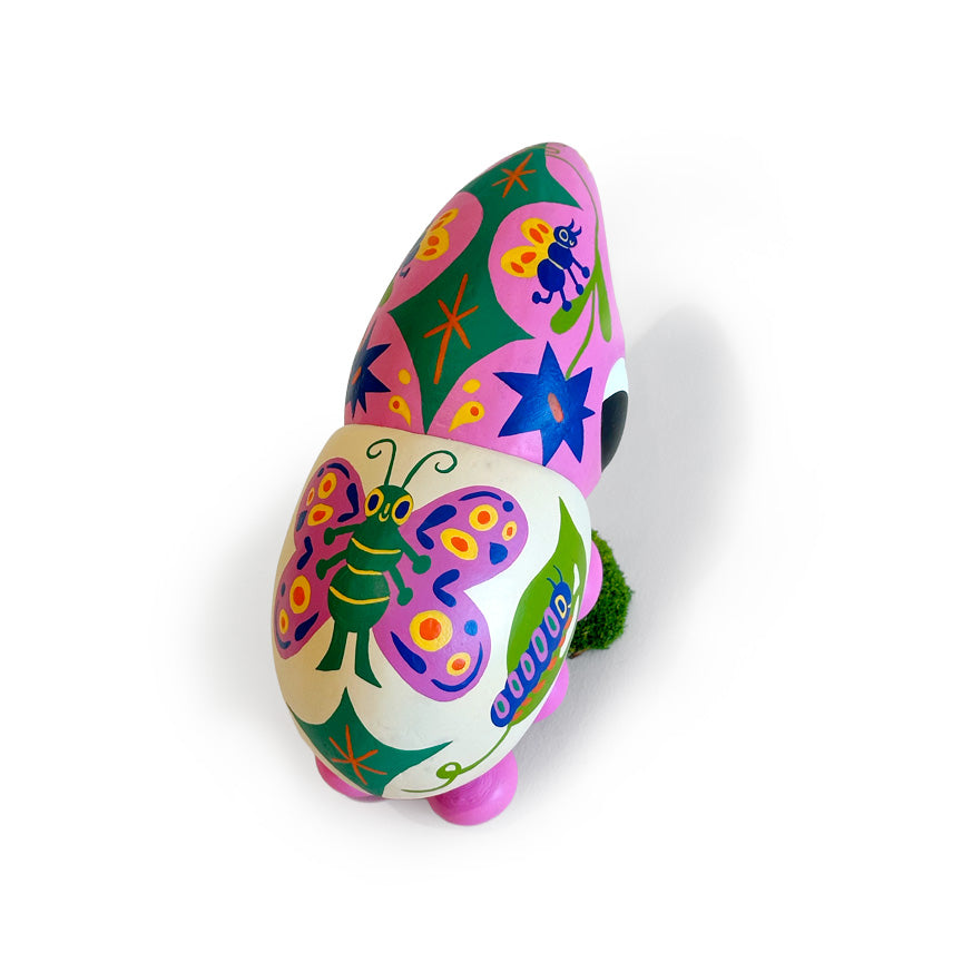 A colorful beetle sculpture with hand-painted floral and insect motifs in pink, green, purple, blue, yellow, and white, standing on a small green mossy base against a plain white background.