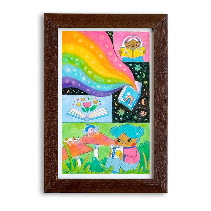 A framed art print featuring whimsical illustrations with a bright rainbow pouring out of book, a girl reading, and another girl reading to a cat and fairy sitting on mushrooms, presented in a dark brown wood frame on a white background.