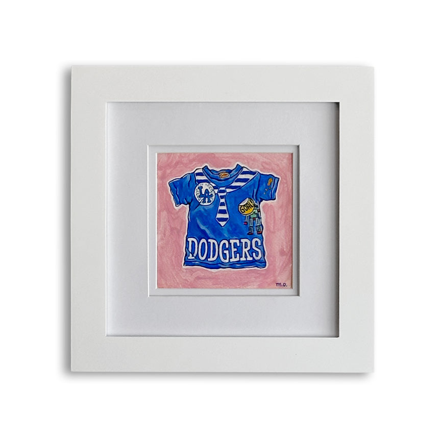 A framed art print featuring a  blue and white baseball jersey with "DODGERS" written on it and stitched necktie and robot patches, set against a pink background and enclosed in a white frame with a white mat.