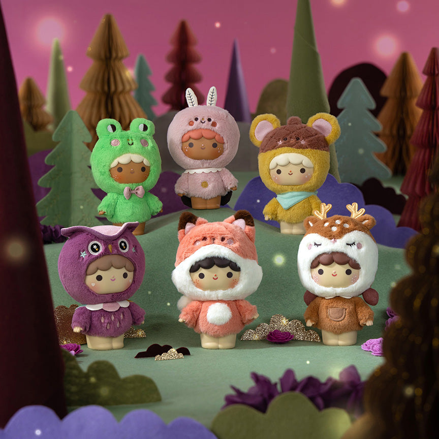Six plush character toys dressed in animal and fantasy costumes, such as a moth, frog, fox, and more, arranged in a whimsical forest scene with layered paper trees and purple foliage. 