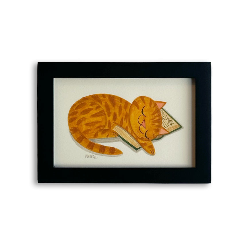 A framed art print featuring a stylized orange tabby cat curled up asleep on a book, set in a black frame against a white background.