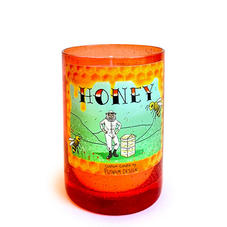Orange glass candle with illustrated decorative label and the text "Honey custom candle by Putnam Design" on a white background. 