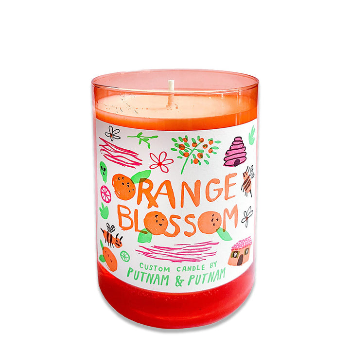 Orange glass candle with illustrated decorative label and the text "Orange Blossom custom candle by Putnam Design" on a white background