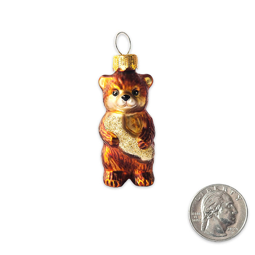 A molded-glass ornament in the shape of a small brown bear hugging the a glittery gold version of the state of California, next to a quarter for size reference. The quarter is about half the size of the ornament. 
