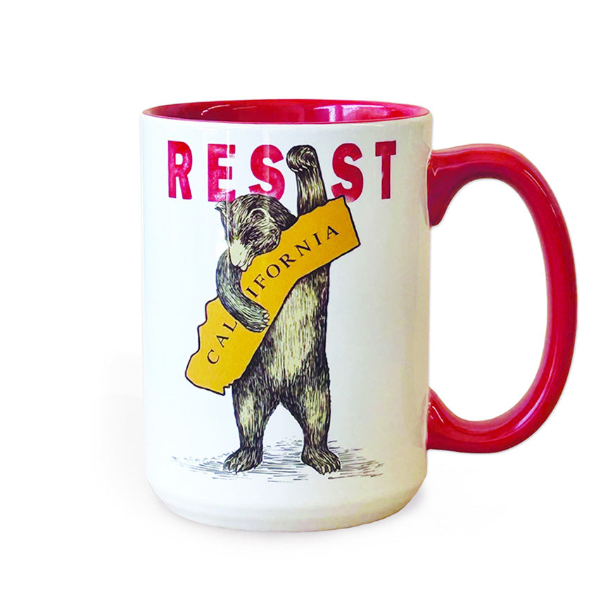 A white ceramic mug with a red handle, red interior, and red letters o the word "resist". On the mug is a bear holding the state of California holding it's fist up. It's fist creates the "i" in the word "resist".