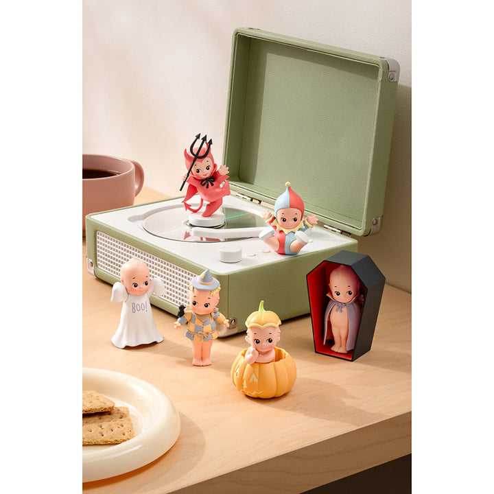 A collection of whimsical cherub figurines all wearing different halloween costumes (devil, jester, ghost, pumpkin, scarecrow, and vampire) displayed on a wooden tabletop next to a record player.