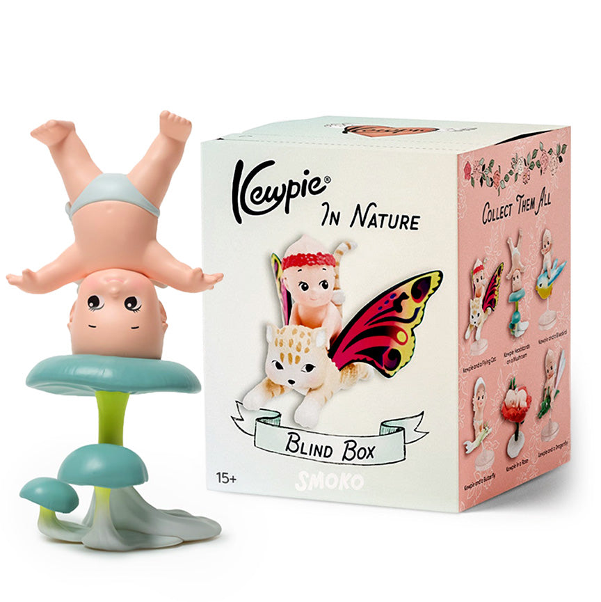 Kewpie figure next to it's packaging, titled "Kewpie in Nature". On the packaging is a picture of a small cherub figure riding a tiger with butterfly wings. The figure next to the box is another Kewpie cherub figure wearing a diaper, standing on it's head on a blue mushroom. 