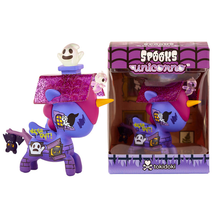 A Tokidoki Spooks Unicorno collectible figure shown next to its retail packaging. The figure is purple and pink with a glittery pink roof, featuring Halloween-themed haunted house design, a small ghost figure on top, and a miniature bat hanging from it&