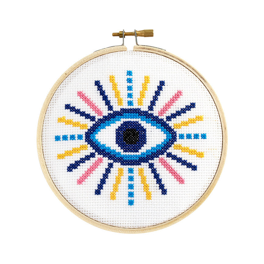 Cross stitch kit depicting a colorful evil eye design on a circular cloth with a hoop.