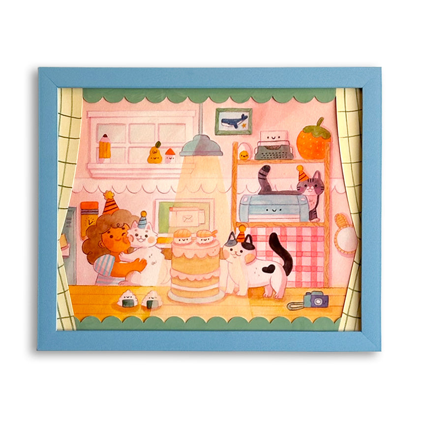 An art print featuring a whimsical illustration of a girl and several cats in a decorated room celebrating a birthday with a cute two-tiered cake. Various objects in the room have cute smiley faces on them. The piece is in a light blue frame against a white background.