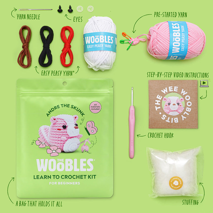 All materials included in Wooble kit (yarn needle, yarn, plastic eyes, pink crochet hook, instructions, stuffing, and reusable zip bag) on a green background. 