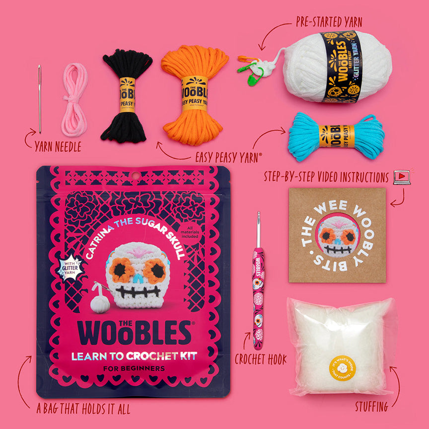 All materials included in Wooble kit (yarn needle, yarn, themed crochet hook, instructions, stuffing, and reusable zip bag) on a pink background. 