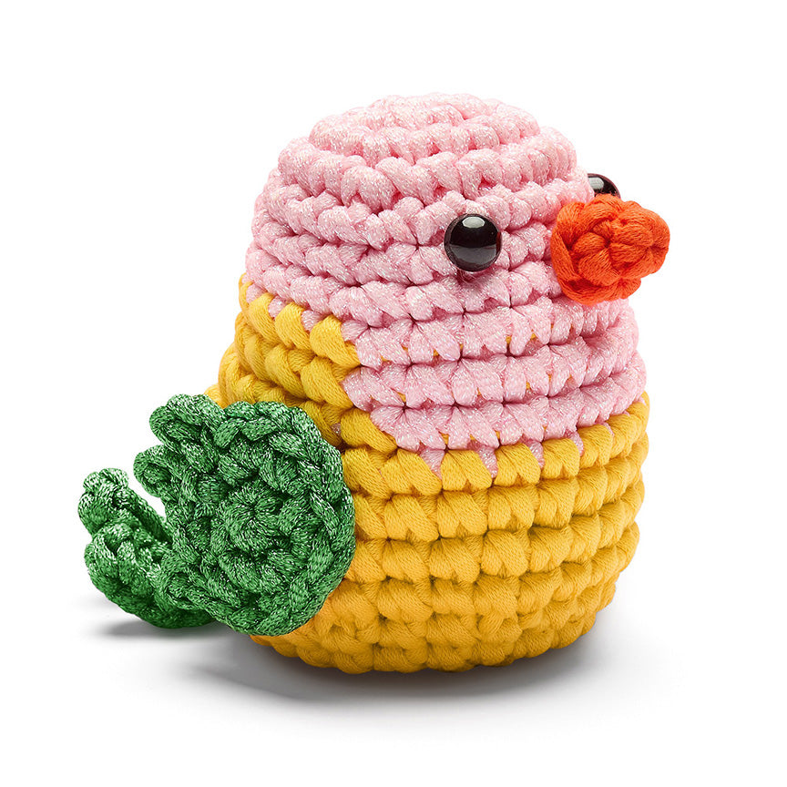 Finished crochet— a small bird with a black plastic eyes, pink head, yellow body, green wings and tail, and orange beak. 