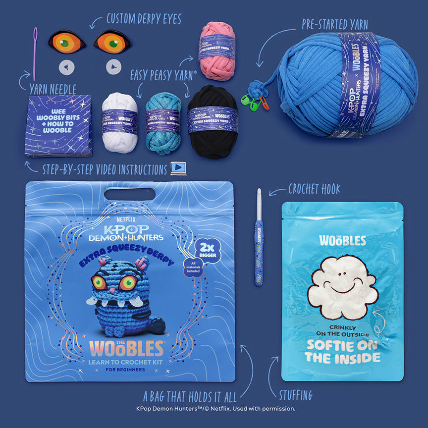 All materials included in Wooble kit (yarn needle, yarn, custom plastic eyes, themed crochet hook, instructions, stuffing, and reusable zip bag) on a blue background. 