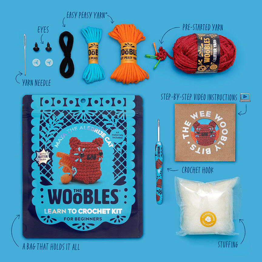 All materials included in Wooble kit (yarn needle, yarn, plastic eyes, themed crochet hook, instructions, stuffing, and reusable zip bag) on a blue background. 