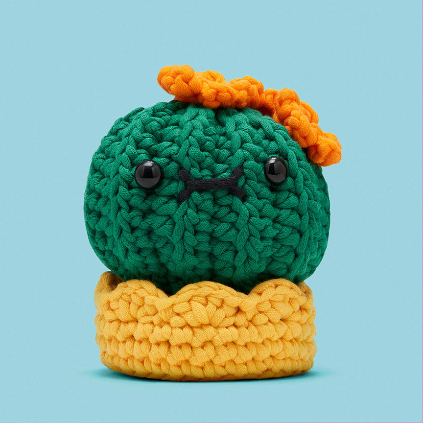 Crocheted cactus toy with a yellow base and orange flower on a light blue background.