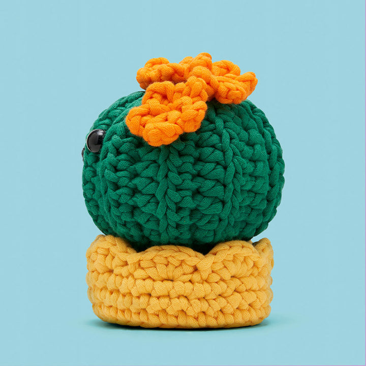 Back of a crocheted cactus toy with a yellow base and orange flower on a light blue background.