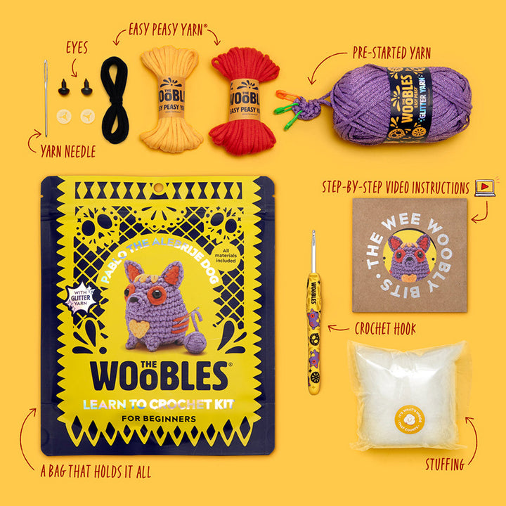 All materials included in Wooble kit (yarn needle, yarn, plastic eyes, themed crochet hook, instructions, stuffing, and reusable zip bag) on a yellow background. 