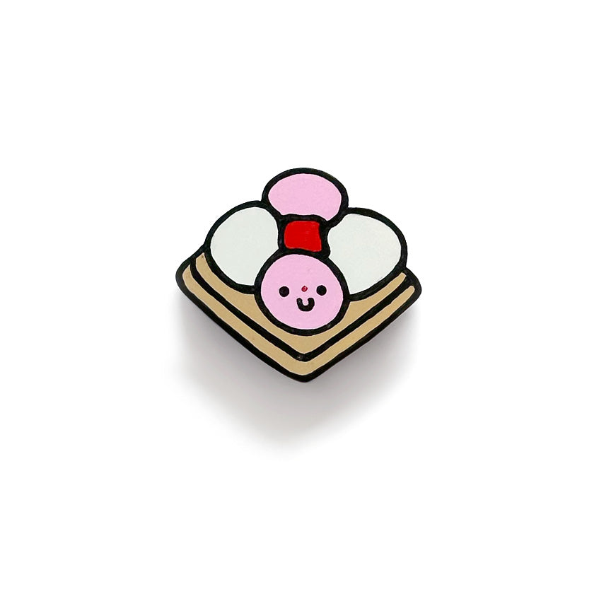 A cute art piece of a carita de bon bon, with pink and white balls on a tan square cookie and a smiley face on one of the balls, against a white background.